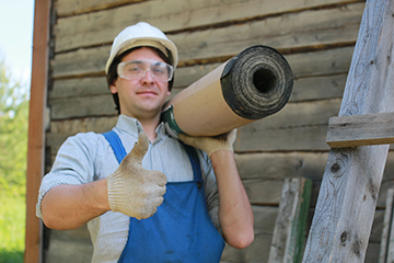 A worker carries a roll of commercial roofing material