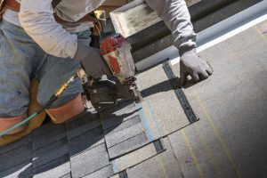 Person using a nail gun installing asphalt roof