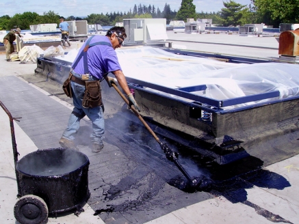 A McDonald & Wetle employee spreads bitumen on a commercial roof